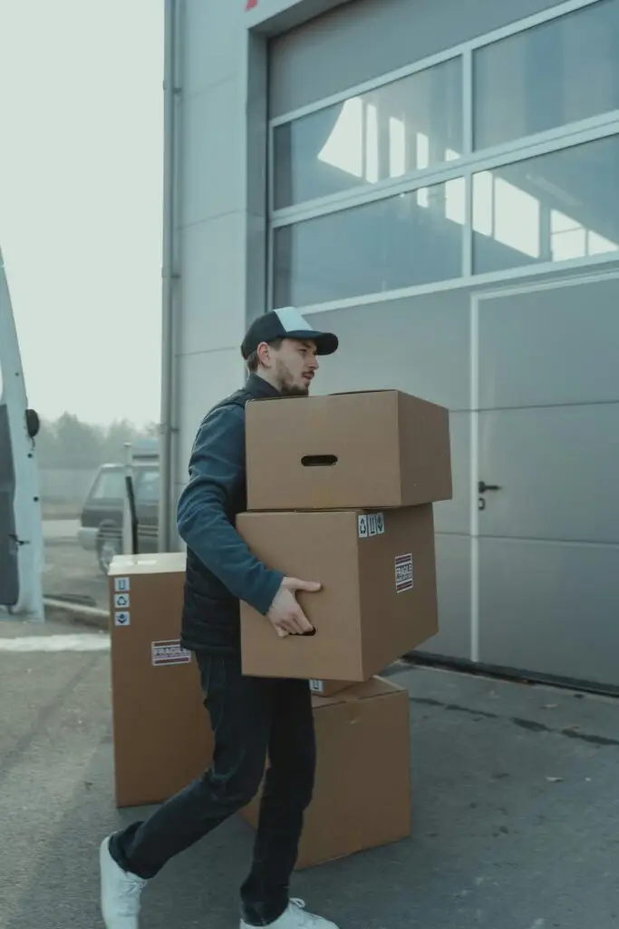 A delivery man carrying cardboard boxes to a loading dock outside an industrial building.